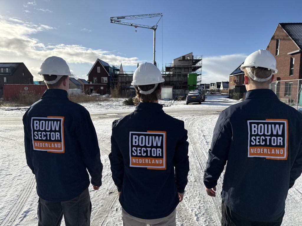 Drie vakmensen van Bouwsector Nederland met helm op een besneeuwde bouwplaats met nieuwe woningen